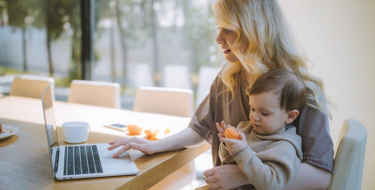 Person holding child while working on laptop